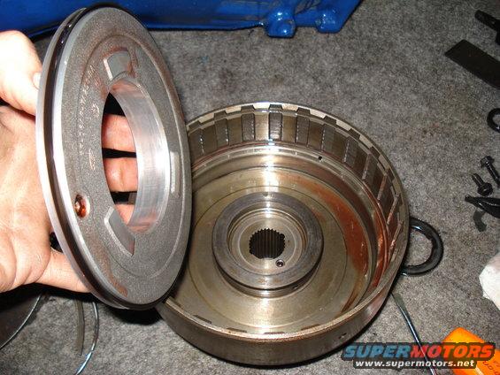Disassembled transmission torque converter part with splined shaft and metal fins. A hand holds a circular metal component