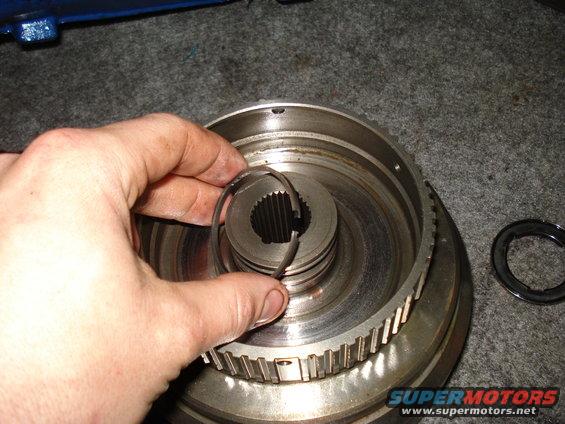 Hand holding snap ring over transmission component. Supermotors.net logo visible