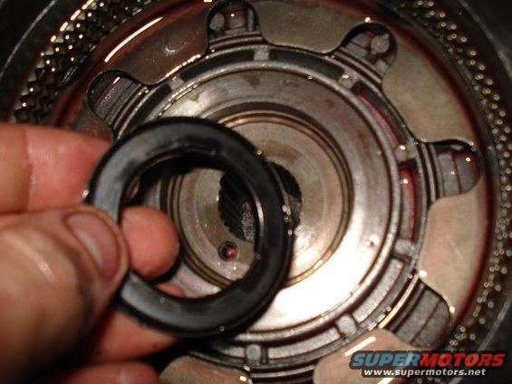 Hand holding a black seal over a metal transmission component with gears visible