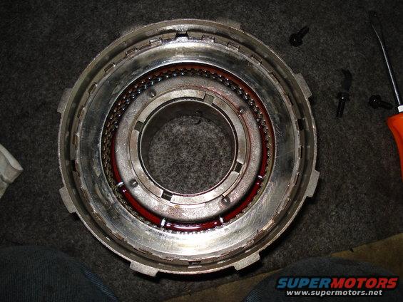 Close-up of a transmission drum with ball bearings and red fluid. A screwdriver is visible on the right