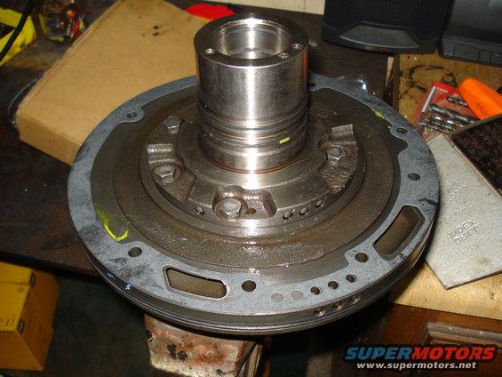 Close-up of a transmission torque converter assembly on a workbench, with tools and boxes in the background