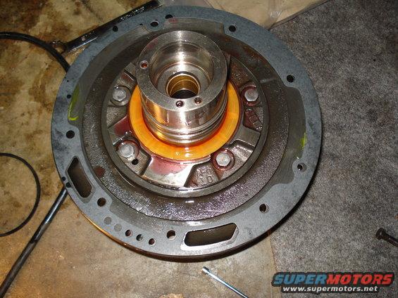Transmission pump assembly with orange seal and metal components, covered in reddish fluid