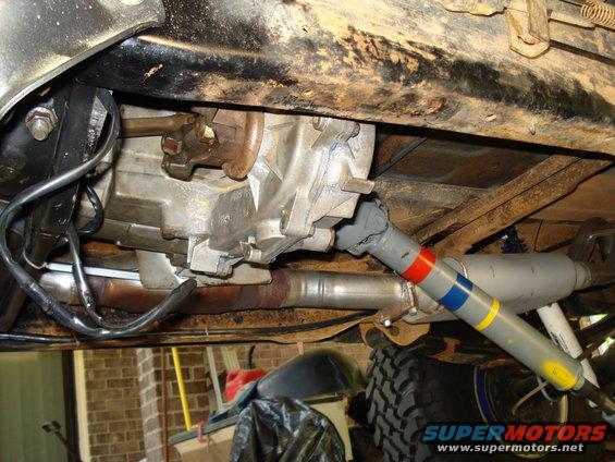 Vehicle underbody showing transmission, driveshaft, and exhaust components. A large tire is visible on the right