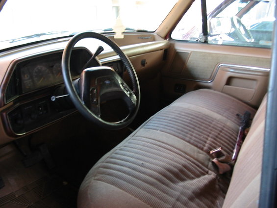 Interior of a 1992 Ford F-150, showing the driver's seat, dashboard, and steering wheel. The upholstery is striped brown and tan