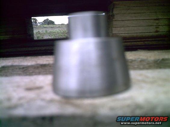 Metal exhaust tip with a view of a field through a dark opening