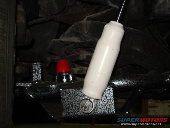 Close-up of a white shock absorber mounted to a black metal bracket with a red cap on a bolt