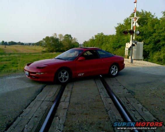 Red 1993 Ford Probe GT parked on railroad tracks, side view