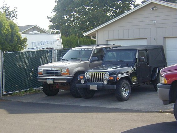 1994 Ford Explorer parked next to a black Jeep Wrangler, with a trailer and garage in the background