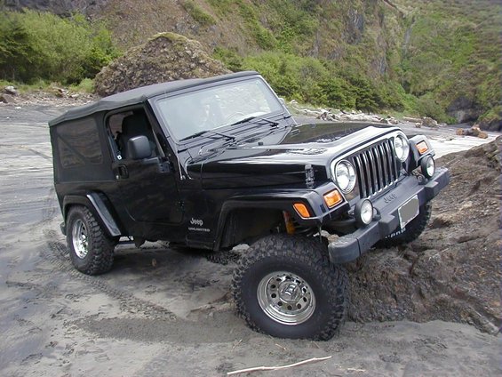 Black Jeep Wrangler with soft top on sandy and rocky ground
