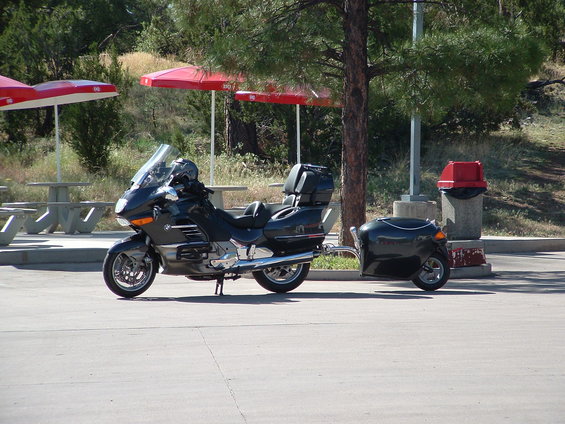 Black BMW motorcycle with trailer, parked outdoors near picnic tables and red umbrellas