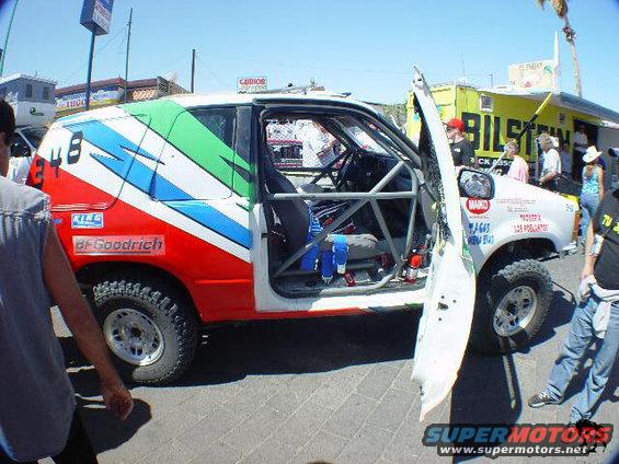 Off-road SUV with racing decals, roll cage visible inside, driver's door open