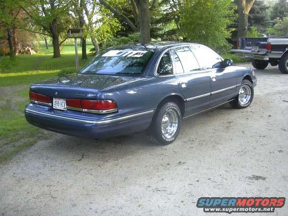Blue 1996 Ford Crown Victoria parked on a dirt road with a pickup truck in the background