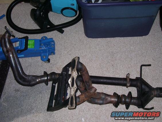 Car exhaust manifold and pipe assembly on carpet with a blue jack and vacuum cleaner