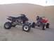 2005 Honda TRX 450 R - Two ATVs are parked in a sandy desert, with dunes in the background and a watermark at the bottom right.