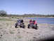 2005 Honda TRX 450 R - Two ATVs are parked on the shore of a lake under a clear blue sky.