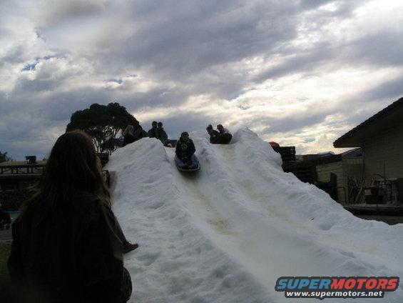 People sledding down a snow hill under a cloudy sky