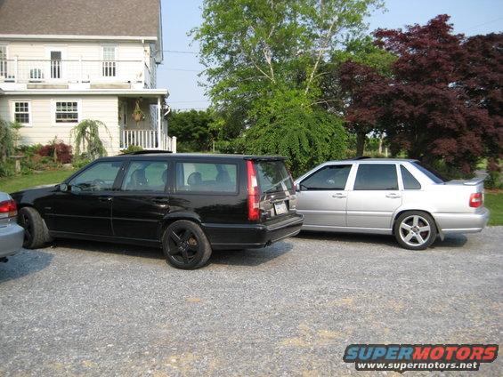Black Volvo wagon and silver Volvo sedan parked in gravel driveway next to a house