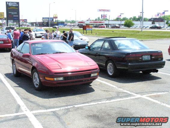 Red Ford Probe parked next to a black Mazda MX-6 in a parking lot