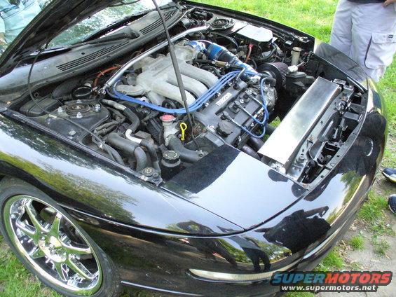 Black car engine bay with V6 engine, chrome rims, and a Supermotors.net watermark