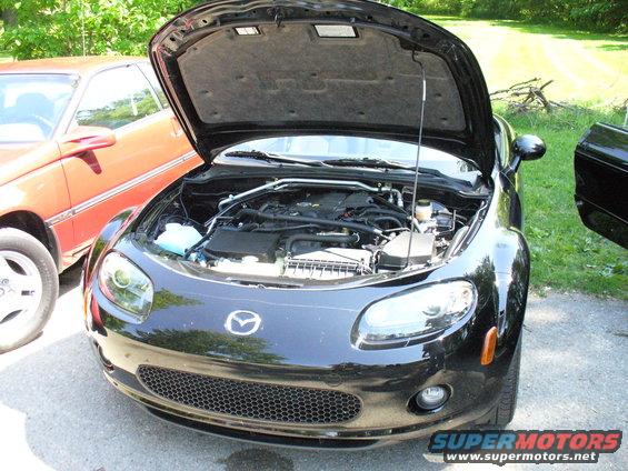 black Mazda MX-5 Miata, hood open showing engine bay, parked next to an orange car