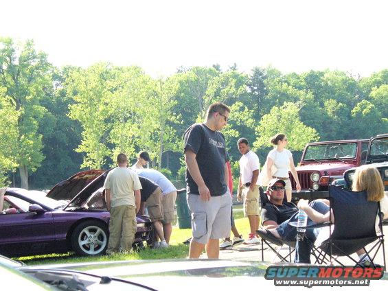 Purple sports car with hood open, people gathered around it. Two Jeeps visible in background
