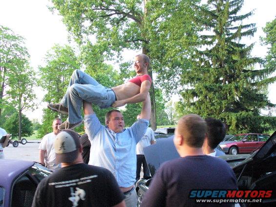 guy lifting another guy over his head, people watching, cars around