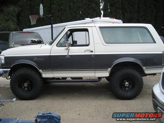Side view of a white and dark gray 1989 Ford Bronco with aftermarket wheels