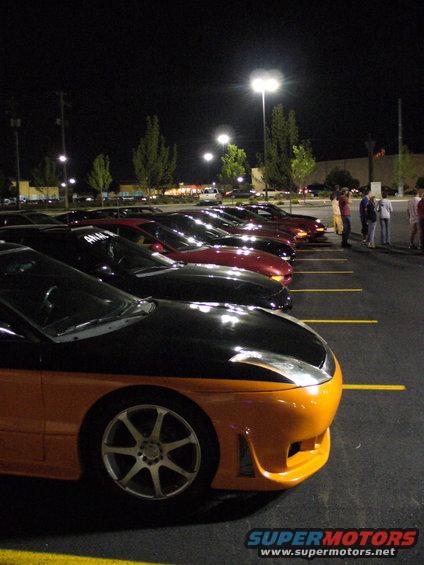 Several cars parked in a lot at night, with a two-tone car in the foreground