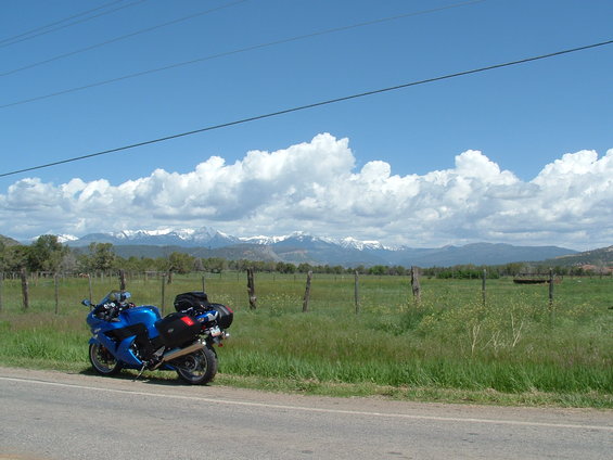 Blue motorcycle parked on roadside with snow-capped mountains behind