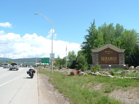 Motorcycle parked on highway shoulder near Durango welcome sign. Other vehicles on road