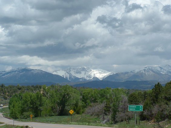 Mountain range under cloudy sky, with a road and green signs indicating Durango and Mancos