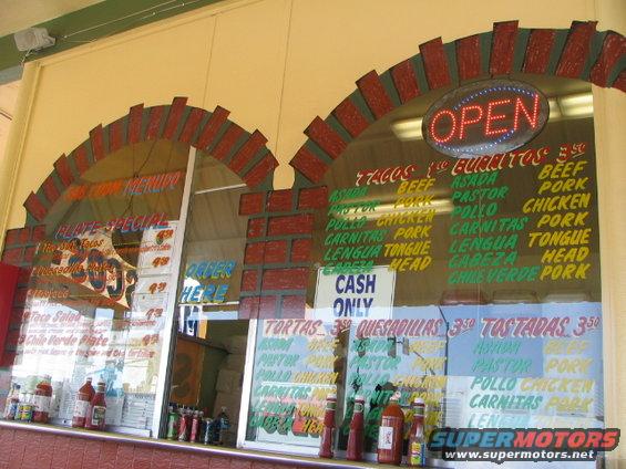 Restaurant window with menus for tacos, burritos, tortas, quesadillas, and tostadas. An "OPEN" sign is illuminated