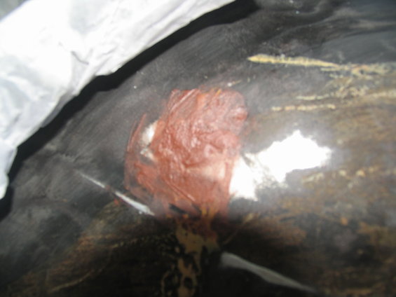 Close-up of a patch of rust-colored material on a dark, possibly rubberized surface, with some white and yellow markings