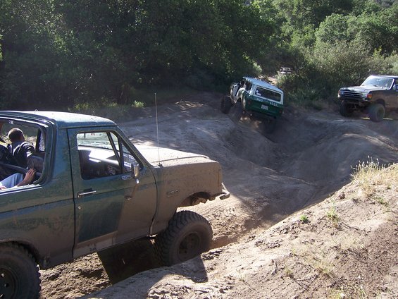Muddy off-road vehicles navigating a steep dirt trail with trees in the background