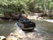 1991 Ford Bronco - A black Toyota Tacoma pickup truck navigates a stream in a wooded area.
