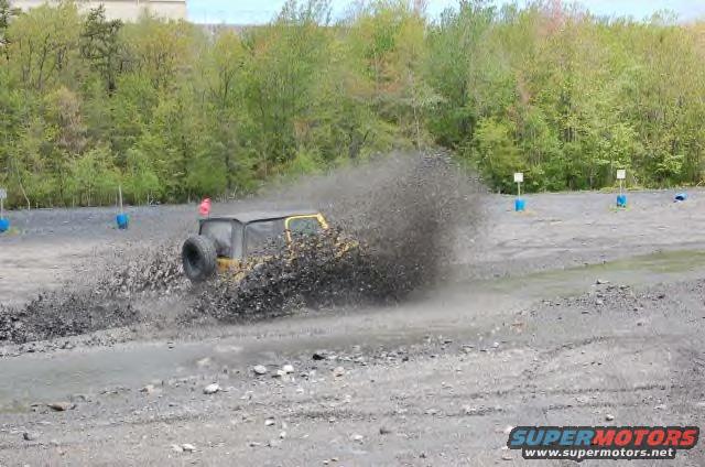 Yellow Jeep Wrangler kicking up mud and rocks on a dirt track