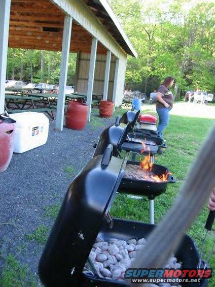 picnic shelter with tables, grills cooking food, and people standing around