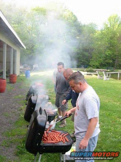 People grilling hot dogs outdoors with smoke rising from grills