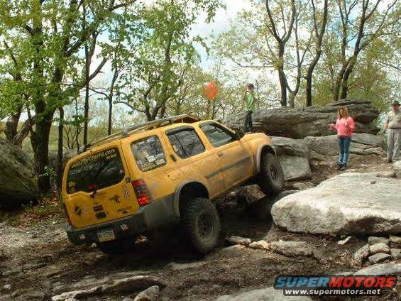 Yellow SUV navigating a rocky off-road trail with people watching