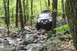 1991 Ford Bronco - An off-road SUV with a roof rack tackles a challenging rocky path through a dense forest.