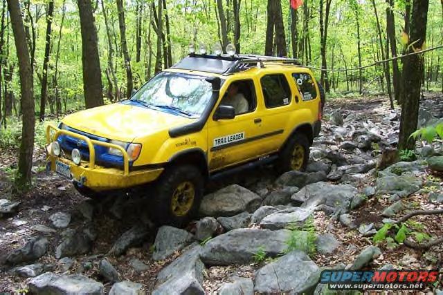 Yellow SUV with snorkel and roof rack navigating a rocky forest trail