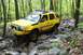 1991 Ford Bronco - A yellow SUV, modified for off-roading with a snorkel and roof rack, tackles a challenging rocky path through a wooded area.