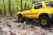 1991 Ford Bronco - Yellow SUV navigates a challenging rocky path through a wooded area.