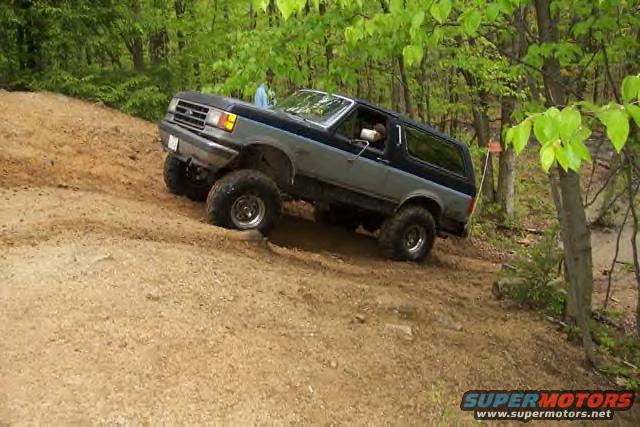 Two-tone Ford Bronco climbing a dirt hill off-road