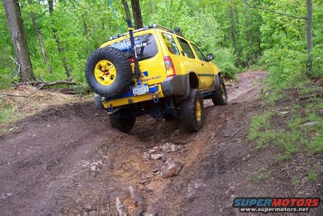 Yellow SUV with spare tire on back driving on a muddy, wooded trail