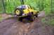 1991 Ford Bronco - Yellow SUV navigates a challenging muddy trail in a wooded area.
