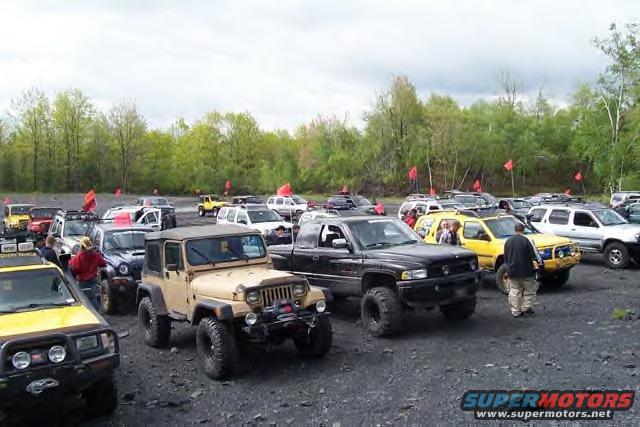 group of Jeeps and trucks parked on gravel lot with trees in background