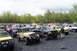 1991 Ford Bronco - Several off-road vehicles are parked together in an outdoor lot, with trees lining the horizon under a cloudy sky.