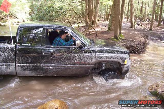 Black pickup truck driving through a muddy stream in a forest