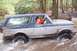 1991 Ford Bronco - A two-tone blue and silver Ford Bronco navigates through a muddy stream in a wooded area.